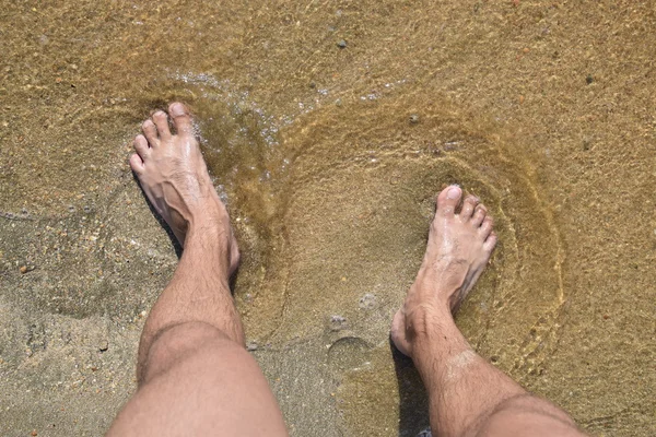 Legs men on the sea sand near sea wave. Walk on the beach.