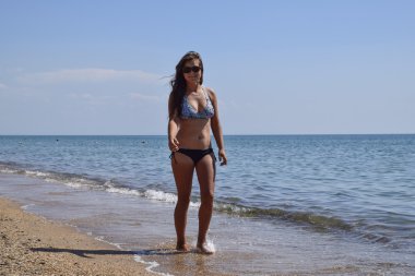 Kız sahilde yürüyüş. Esmer kadın bir mayo kıyı şeridi boyunca deniz sahilde yürümek.