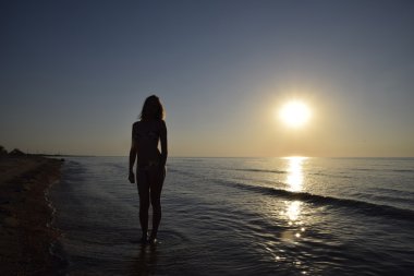 Gün batımına karşı bir kızı deniz kenarında silüeti. Deniz günbatımı karşı karanlık siluet. Kız akşam sahilde.