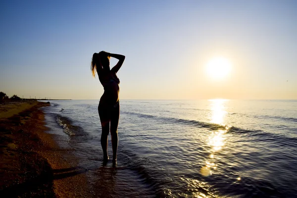 Gün batımına karşı bir kızı deniz kenarında silüeti. Deniz günbatımı karşı karanlık siluet. Kız akşam sahilde.