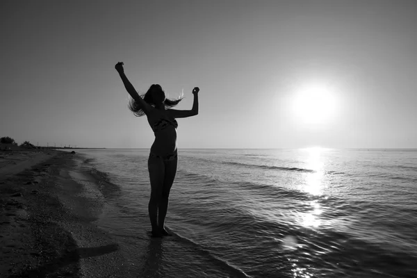 Silhouette of a girl against the sunset by the sea. The dark silhouette against the sea sunset. Girl on the beach in the evening.