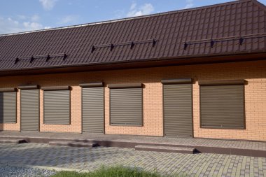 Oluklu levha üzerinde bir binanın çatısı. Kahverengi saclar kiralanan store üzerinde çatı kaplama. Windows üzerinde Brown panjurlar.