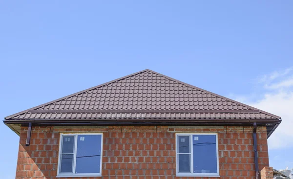 The house with plastic windows and a roof of corrugated sheet. Roofing of metal profile wavy shape on the house with plastic windows.