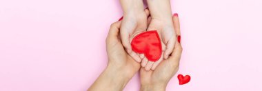 Kırmızı kalp, çocuk ve annenin elleri pembe arka planda. Aşk, hayırseverlik, empati, kopyalama alanı