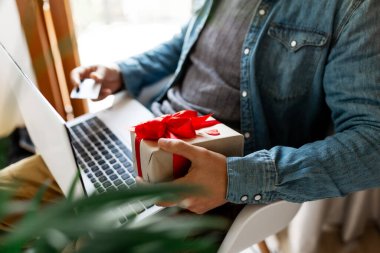 Dizüstü bilgisayar ve kredi kartı kullanan bir adam Sevgililer Günü için hediye sipariş veren bir adam, Kadınlar Günü, Noel. Tatillerde online alışveriş