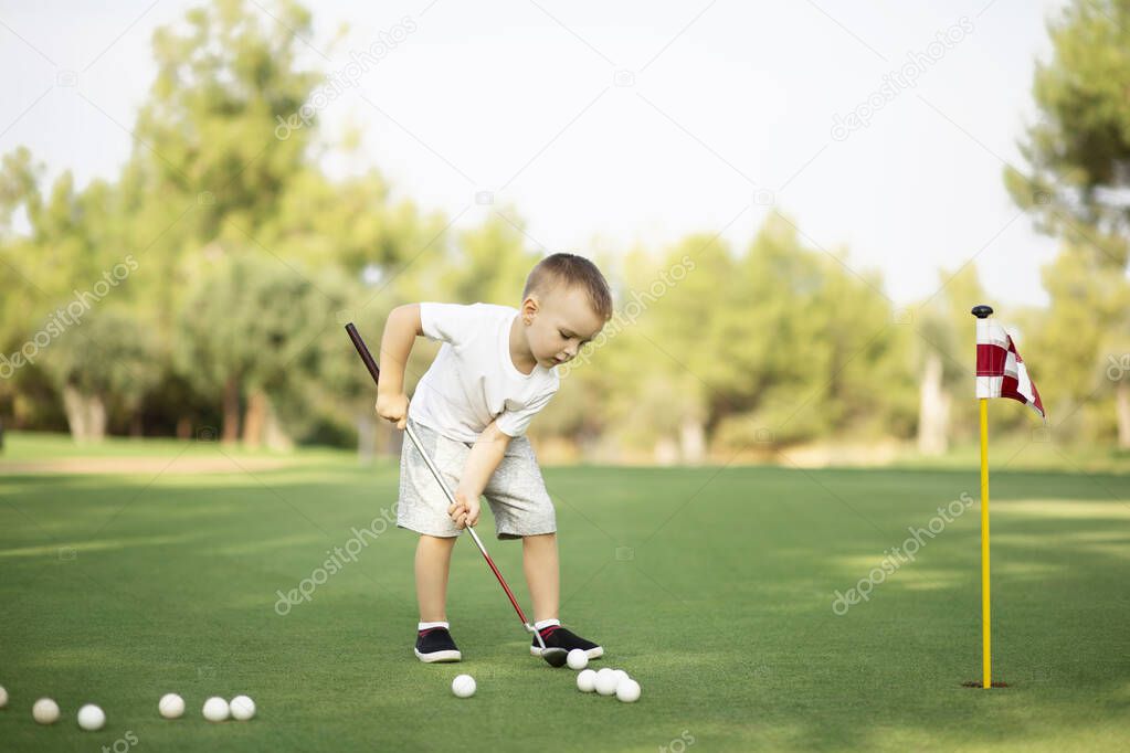 little Boy playing golf and hitting ball by putter on green grass.