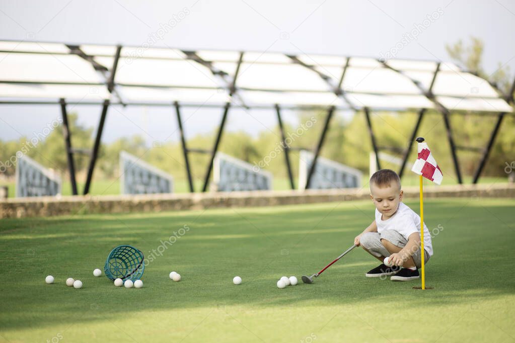 Little boy golfer with his plastic golf set on green field outdoor, collecting his golf balls in bascket