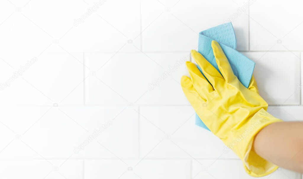 Hand and glove cleaning the bathroom tiles