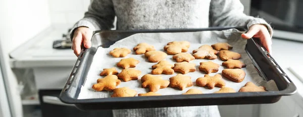 Woman in grey sweater baking ginger breads,holding the baking tray. Christmas holiday fun.