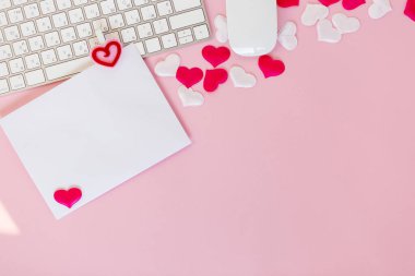 14 Şubat 'taki Sevgililer Günü için beyaz kağıda dilek yaz. Sevgililer gününü pembe arka planda kutlayalım. Ofis dairesi kırmızı oyuncak kalpler ve beyaz klavye ve fare ile yatıyordu, aşk konsepti