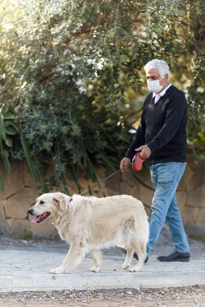 senior man in mask with his pet dog on street because of air pollution and epidemic in city. Protection against virus