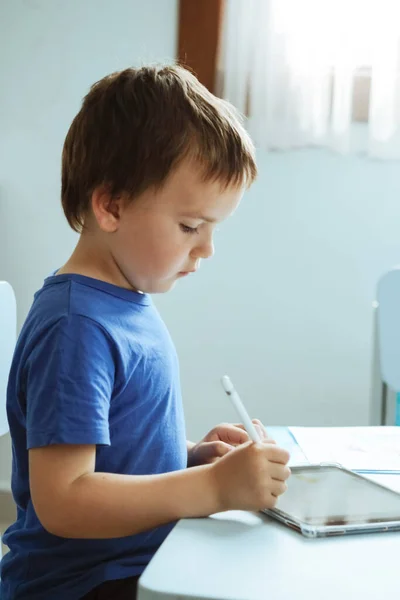 Lindo chico en camiseta azul usando tableta digital o computadora para dibujar su imagen, usando lápiz. Arte de las nuevas tecnologías, educación en línea —  Fotos de Stock