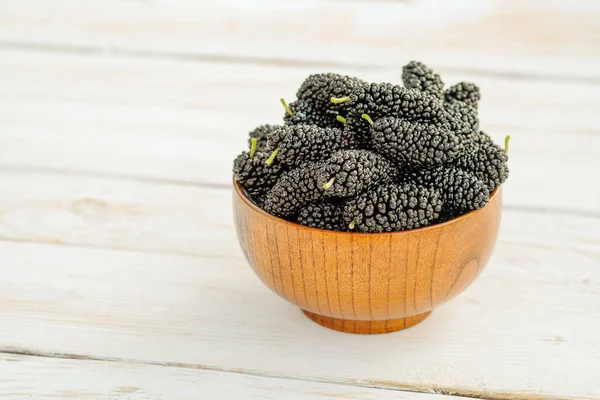 Fresh black mulberry in a wooden bowl on the white wooden table. Mulberry close-up. Organik freshly harvested berries.Side view,copy space — Stock Photo, Image