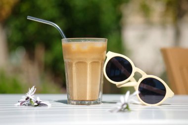 Kıbrıs Rum Kesimi buzlu kahve Frappe Fredo beyaz masada, güneş gözlüklü. Yaz minimalist geçmişi, tatil ya da tatil konsepti. Güneş ve gölgeler.