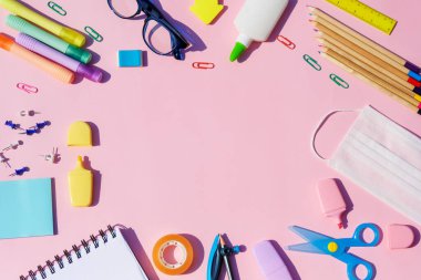 Okulun parlak konseptine, renkli okul malzemelerine sahip çerçeveye, pembe arka planda tıbbi maskeye. 
