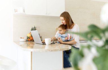 Laptop kullanan bebekli genç bir kadın. Blogcu, yazar, gazeteci, öğrenci kız evde bilgisayar çalışıyor. İş kadını, evden çalışma, uzaktan eğitim, çevrimiçi öğrenme, öğrenim kavramı.