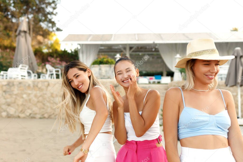 Group of three happy young female friends is having fun and runs at sunset beach to sunlight , laugh and smile.