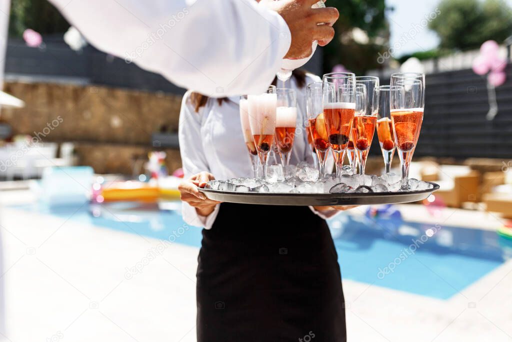 Midsection of waiter pouring champagne at poolside.Serving with ice on a tray. Swimming pool party concept