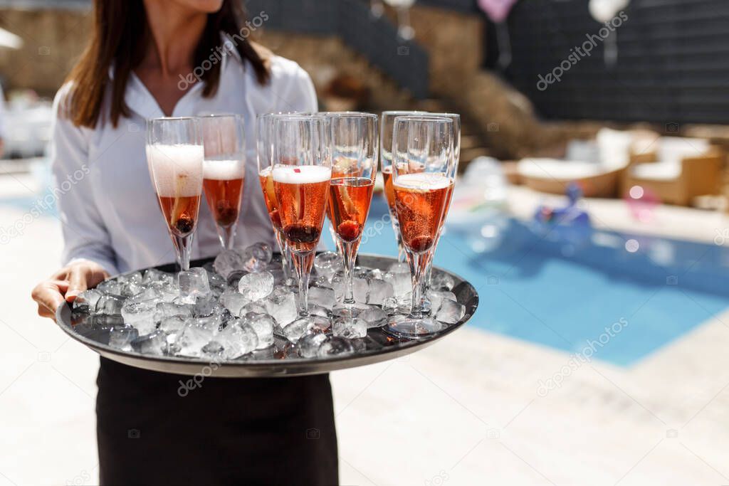 Midsection of waiter offering champagne at poolside.Serving with ice on a tray. Swimming pool party concept