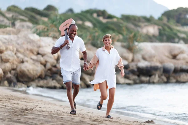 Feliz raça mista, casal de meia-idade abraçando enquanto caminhava na praia segurando uma guitarra. Homem segurando guitarra com mulher — Fotografia de Stock