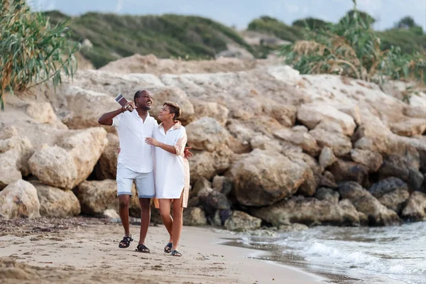 Feliz raça mista, casal de meia-idade abraçando enquanto caminhava na praia segurando uma guitarra. Homem segurando guitarra com mulher — Fotografia de Stock