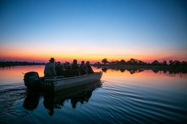 Botswana 'nın Okavango Deltası' nda insanlar gün batımında teknede..