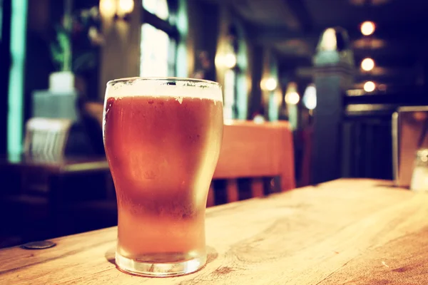 Zbliżenie szklanki świeżych spienionym piwem na stole w vintage rozmycie — Zdjęcie stockowe