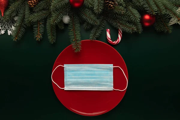 Masada Noel süsüsüyle süslenmiş tıbbi maskeli bir tabak var. Salgının Noel kutlaması üzerindeki etkisinin kavramsal fotoğrafı.