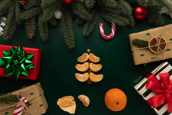 Noel ağacı şeklinde katlanmış mandalina dilimleri Noel süsüyle süslenmiş bir masanın üzerinde yatıyor..