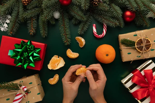 Bir adam Noel süsüsüyle süslenmiş bir masada mandalina soyar..