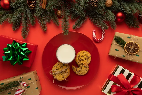 Bir tabak ev yapımı kurabiye ve Noel süsüsüyle süslenmiş bir bardak süt var..