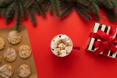 Noel süsüsüyle süslenmiş bir masada, içinde şekerlemeler ve Noel kurabiyeleri olan bir fincan sıcak çikolata var..