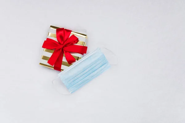 Covid-19 virüsünün tatillerin kutlanması üzerindeki etkisinin kavramsal fotoğrafı. Bir Noel hediyesi ve kar altında bir tıbbi maske..