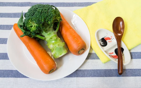 Duas cenouras e brócolis na placa branca com colher de madeira — Fotografia de Stock