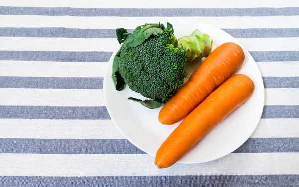 Brócoli y dos zanahorias en la placa blanca colocada en rayas blancas — Foto de Stock