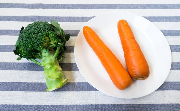 Doi morcovi pe placa alba cu broccoli verde pe albastru si alb — Fotografie, imagine de stoc