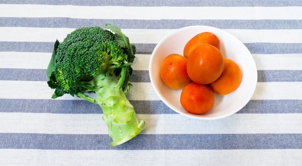 Pět rajčata na bílé misce s brokolicí na proužkovaném pozadí — Stock fotografie