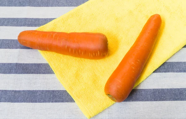 Deux carottes placées sur un tissu doux jaune avec fond rayé — Photo