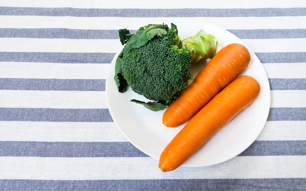 Broccoli och två morötter på vit platta ut på vit randig Stockbild