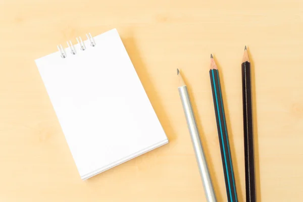 Drie potloden met witte Notebook op licht bruin houten tafel — Stockfoto