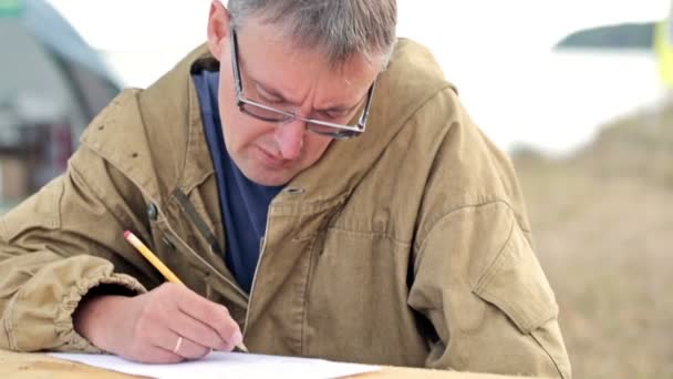 Hombre poeta o escritor escribe una nueva obra, verso o poema. Tal vez escribió una carta a su esposa o familia. Parece un pescador o un cazador. . — Vídeos de Stock