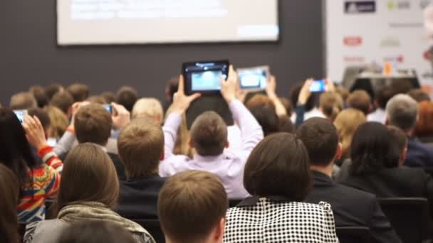 Les personnes présentes à une conférence ou à une présentation, à un atelier, à une photographie en classe de maître, aux gadgets d'image font des smartphones et des tablettes . — Video