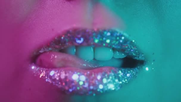Női ajkak neon ultraibolya fényben. Divatos neonfény, eufória. A szexi lány a nyelvével nyalogatja a fogait. Fényes ajkak egy nightclubban. Rózsaszín-kék-zöld szín és új fény. Fémrúzsok — Stock videók