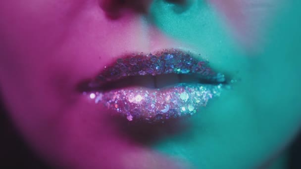 Neon ultraviyole ışıktaki kadın dudaklar. Moda neon ışığı, coşku. Seksi kız dişlerini diliyle yalıyor. Gece kulübünde parlak dudaklar. Pembe-mavi-yeşil renk ve yeni ışık. Metalik ruj — Stok video