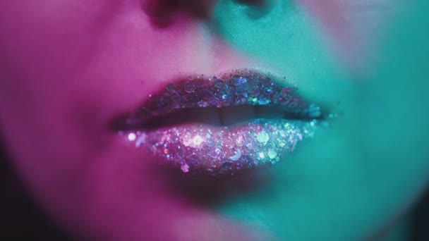 Labios femeninos en luz ultravioleta de neón. Luz de neón de moda, euforia. Sexy chica lame sus dientes con su lengua. Labios brillantes en un club nocturno. Color rosa-azul-verde y nueva luz. Lápiz labial metálico — Vídeo de stock