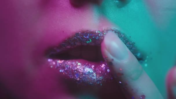 Millennial-Mädchen im trendigen Neonlicht. In einem Nachtclub wischte sie sich mit der Hand die Lippen ab. Glänzendes Glitzer-Make-up auf den Lippen, lächelnd. Modisch gefärbtes rosa-grünes Licht, Euphorie — Stockvideo