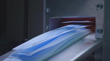 Tıbbi maske üretimi. Maske bir makineden ya da konveyör hattından karton bir kutuya düşer. Pandemik ya da karantina sırasında tıbbi materyal üretimi. Koronavirüse karşı koruyucu maskeler.