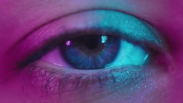 Zbliżyć ujęcie otworu oka niebieską tęczówką. Zdrowy wzrok. Niebieskie oko kobiety w neonowym świetle. Młoda seksowna dziewczyna w nocnym klubie. Makro spojrzenie ludzkiego oka. Różowo-niebiesko-zielony kolor, euforia — Wideo stockowe