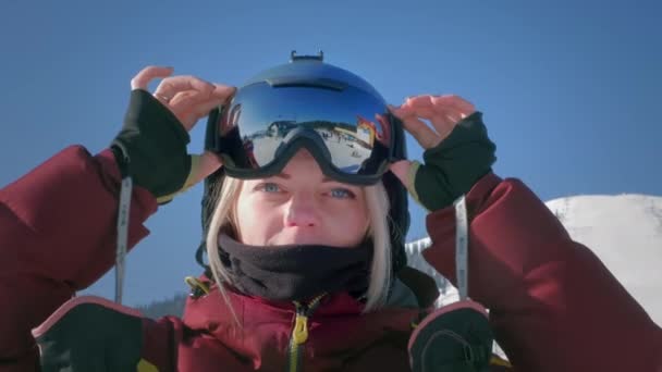 Piękna dziewczyna zakłada zimowe gogle lub maskę do snowboardu. Koncepcja zwycięstwa w sporcie, wygranej, wygranej. Przygotowuję się do jazdy na nartach na zaśnieżonym stoku. Zimowa podróż w ośrodku narciarskim — Wideo stockowe