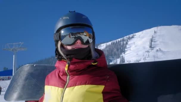 Portret van een mooi meisje dat naar de berghelling kijkt. Een toerist in een masker of snowboardbril kijkt vooruit. Het concept van overwinning in de sport. Winterreizen in het skigebied — Stockvideo